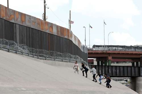 Migrantes caminan frente al muro fronterizo entre México y Estados Unidos, cerca del Puente Internacional Santa Fe, en Ciudad Juárez, estado de Chihuahua, México, el 11 de mayo de 2019.