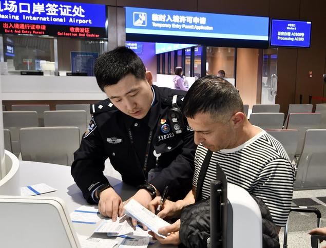 Imagen del 27 de diciembre de 2024 de un turista extranjero llenando una tarjeta de entrada temporal con la ayuda de un oficial de policía en un puesto de control fronterizo en el Aeropuerto Internacional Daxing de Beijing, en Beijing, capital de China. (Xinhua/Ju Huanzong)