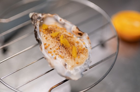 Ostra al estilo Ducasse Paris con mayonesa de leche de soja y miel gratinada, polen y pulpa de naranja.